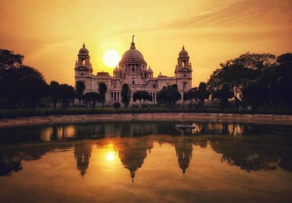 A breathtaking sunset over the Victoria Memorial in Kolkata, India. The iconic white marble structure is reflected beautifully in the still waters of the surrounding pond.