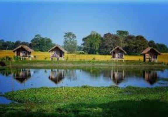 Traditional thatched huts reflected in a serene lake in Majuli, Assam.