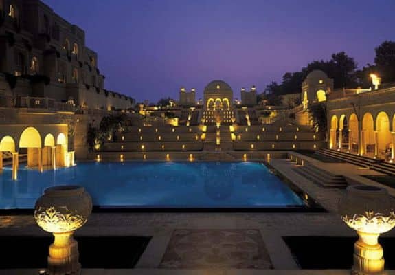 Night view of The Oberoi Amarvilas in Agra, showcasing a stunning illuminated pool, grand architecture, and serene surroundings under a deep blue sky.