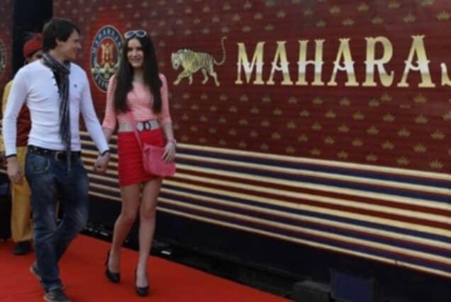 A couple walking hand in hand on the red carpet in front of the luxurious Maharajas' Express train, India, a symbol of royal travel.