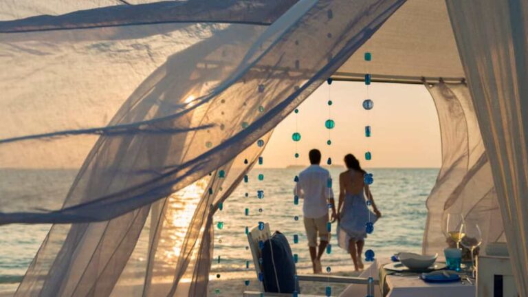 A couple walking hand-in-hand by the beach during sunset