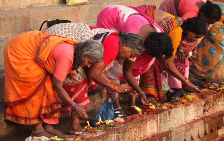 Women performing traditional rituals with offerings and lamps on the ghats of Varanasi, Uttar Pradesh, India.